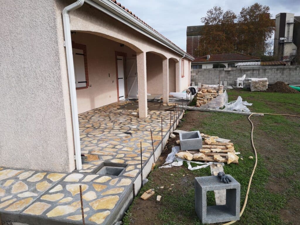 Grande terrasse de maison en pierre naturelle irrégulière, avec patio pavé et jardin. Chantier extérieur, matériaux de construction.