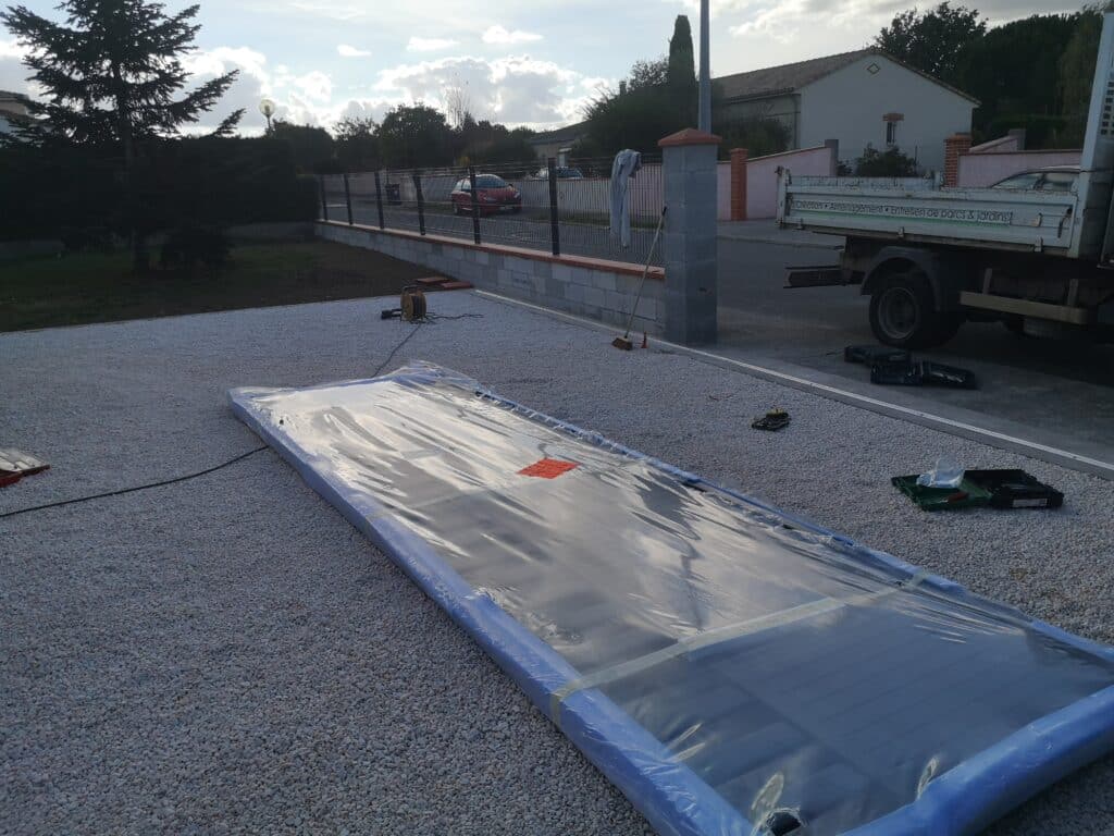 Installation de bâche/panneau solaire sur gravier blanc devant une clôture, avec camion de 'Création • Entretien de parcs & jardins'.